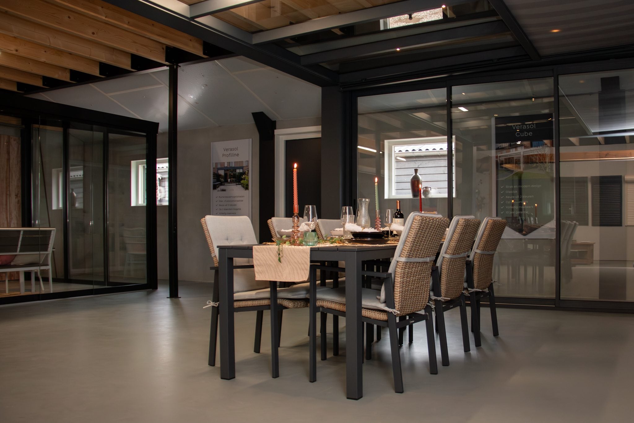 Gedekte eettafel met rieten stoelen onder een overkapping met glazen schuifwanden, in de showroom
