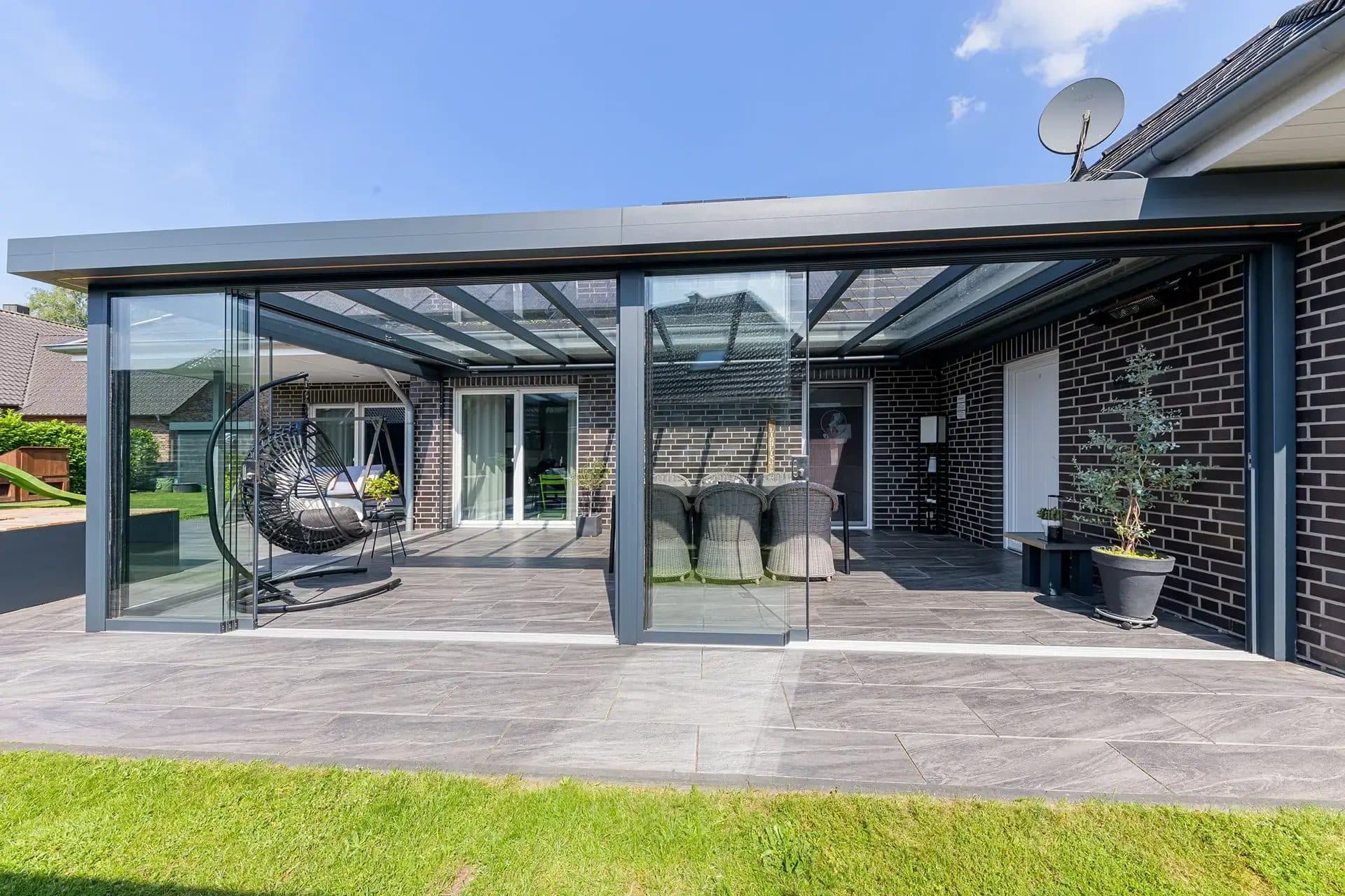 Antraciet veranda met vlak ogend dak en glazen schuifwanden aan een bungalow, met terras en gazon