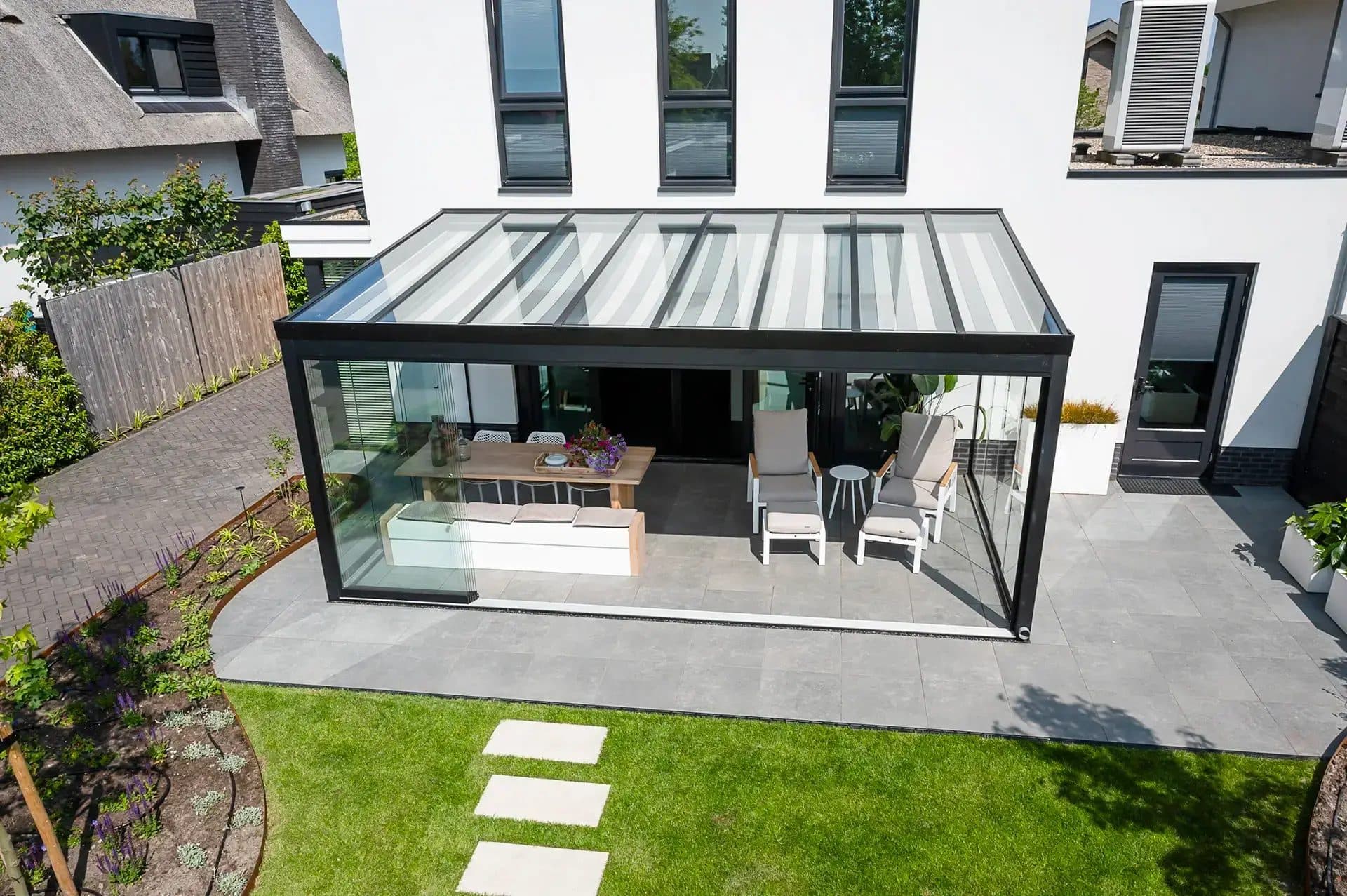 Zwarte veranda met hellend glasdak en glazen wanden aan een witte woning, schuin van bovenaf gezien